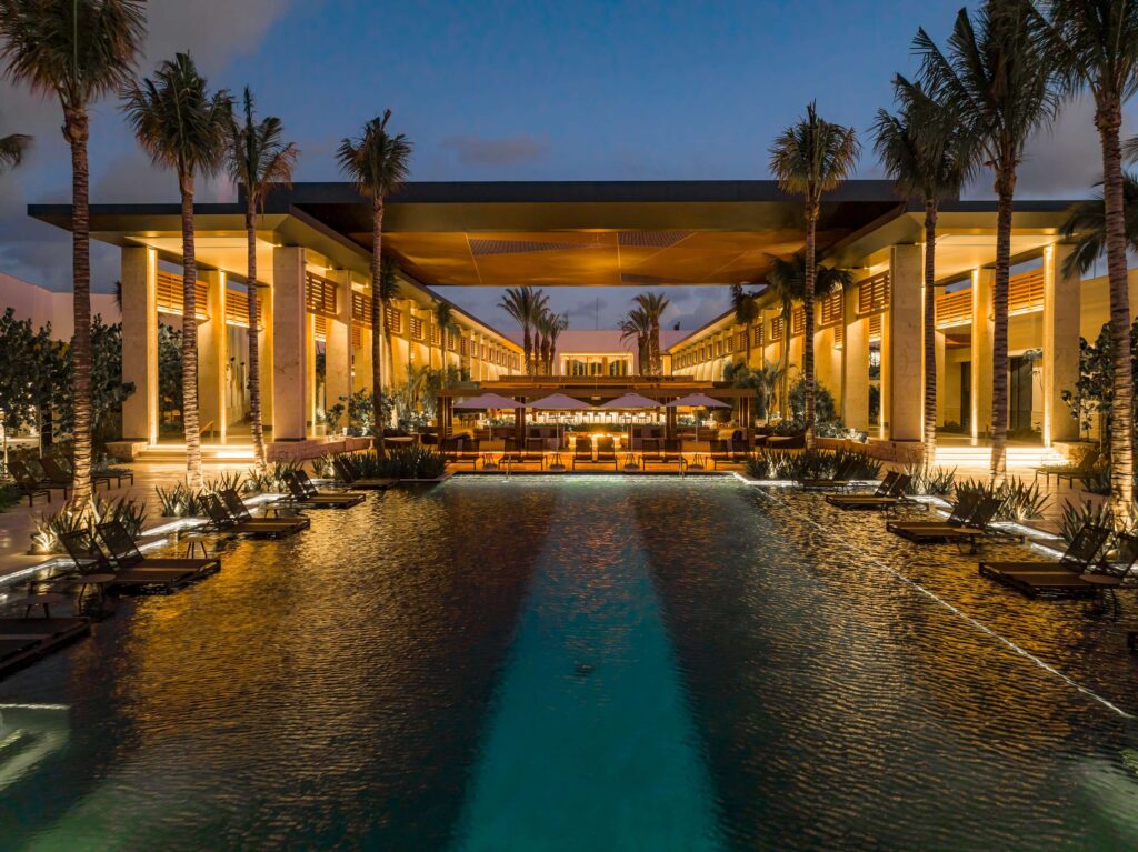 pool at the conrad tulum shown at dusk. the pool is lit up and flanked by loungers and palm trees.