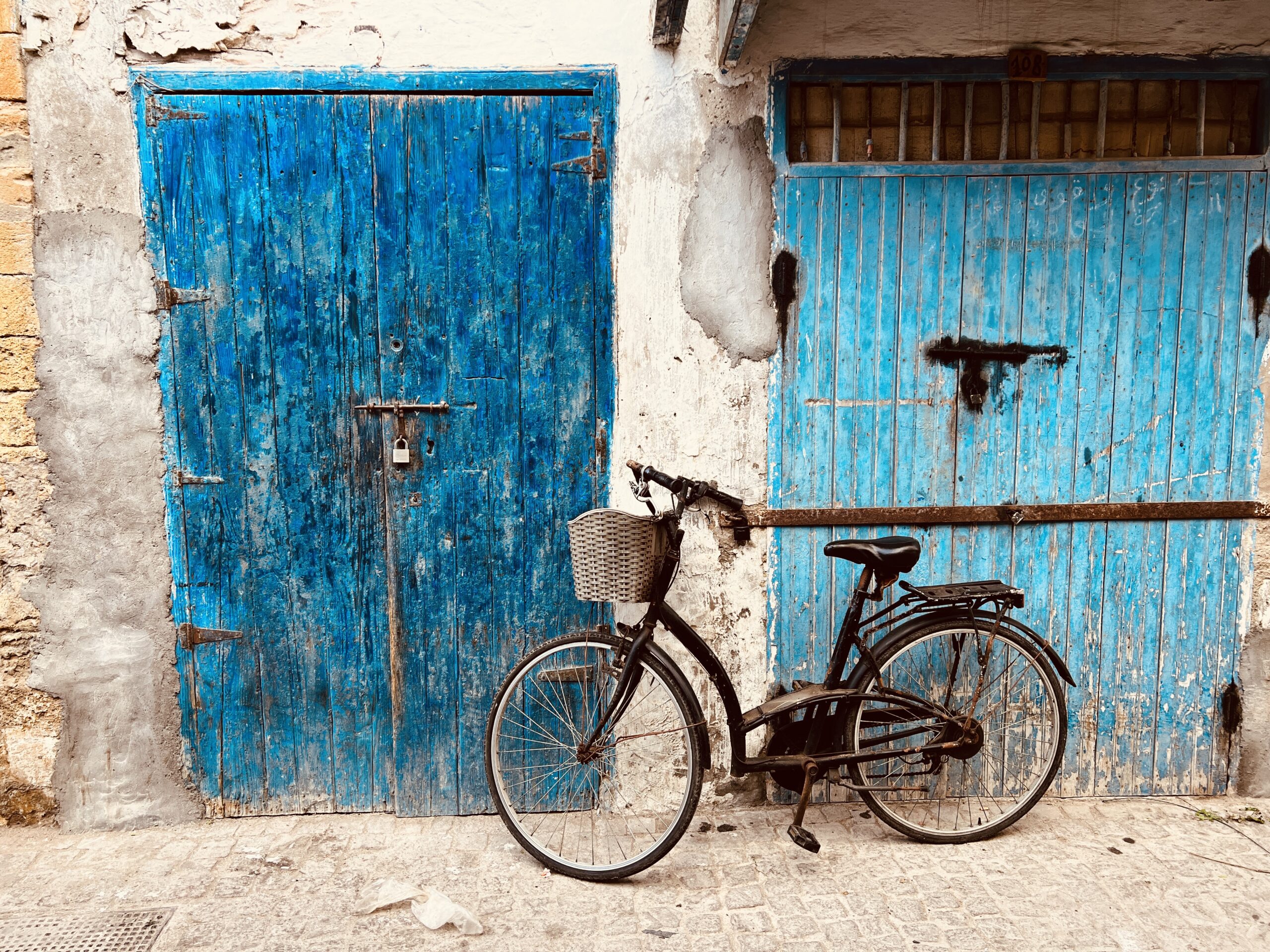 black bicycle with basket propped against a wall that has two weathered blue doors